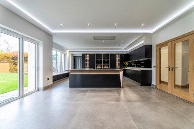Design ideas for a large contemporary l-shaped kitchen pantry in Edinburgh with a built-in sink, flat-panel cabinets, black cabinets, composite countertops, grey splashback, mirror splashback, black appliances, ceramic flooring, an island, beige floors and multicoloured worktops.