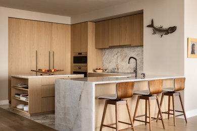 Example of a trendy u-shaped kitchen design in Philadelphia with an undermount sink, flat-panel cabinets, medium tone wood cabinets, beige backsplash, stone slab backsplash, stainless steel appliances, an island and beige countertops