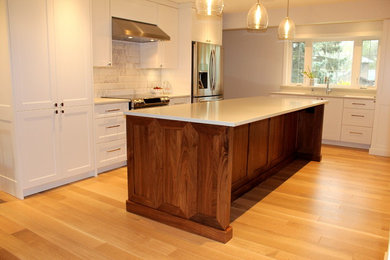 Example of a large transitional l-shaped light wood floor eat-in kitchen design in Other with an undermount sink, shaker cabinets, white cabinets, quartz countertops, white backsplash, ceramic backsplash, stainless steel appliances and an island