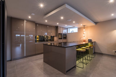 Design ideas for a mid-sized modern eat-in kitchen in Cheshire with a single-bowl sink, grey cabinets, quartzite benchtops, grey splashback, mirror splashback, black appliances, porcelain floors, with island and grey floor.