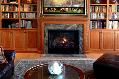 Photo of a traditional family room in Boston with a library, light hardwood floors, a standard fireplace, a wood fireplace surround and a concealed tv.
