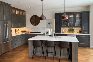 Design ideas for a mid-sized transitional l-shaped open plan kitchen in Denver with an undermount sink, shaker cabinets, grey cabinets, solid surface benchtops, white splashback, marble splashback, stainless steel appliances, medium hardwood floors, with island, multi-coloured floor and white benchtop.