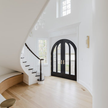 Elegant Foyer Entrance with Arched Black Door and Curved Staircase