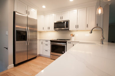 Transitional u-shaped kitchen photo in Omaha with a farmhouse sink, shaker cabinets, white cabinets, quartzite countertops, stainless steel appliances and white countertops