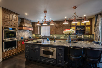 Example of a large trendy u-shaped dark wood floor and brown floor enclosed kitchen design in Other with a farmhouse sink, raised-panel cabinets, brown cabinets, quartz countertops, gray backsplash, ceramic backsplash, stainless steel appliances, an island and multicolored countertops