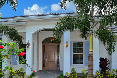 This is an example of a beach style two-storey stucco white house exterior in Tampa with a hip roof and a tile roof.