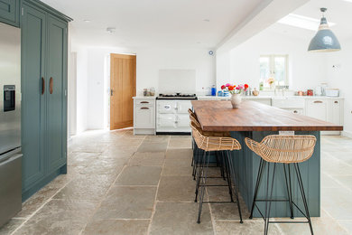 This is an example of a country kitchen in Kent with a farmhouse sink, shaker cabinets, white cabinets, wood benchtops, white appliances, with island and beige floor.