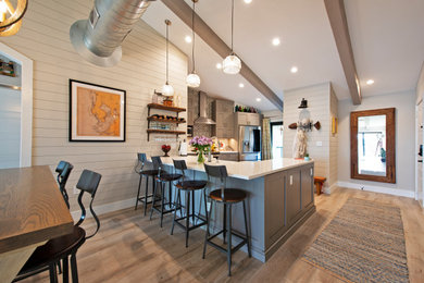Inspiration for a small rustic u-shaped light wood floor, brown floor and exposed beam open concept kitchen remodel in Tampa with a farmhouse sink, beaded inset cabinets, gray cabinets, quartz countertops, blue backsplash, mosaic tile backsplash, stainless steel appliances, an island and white countertops