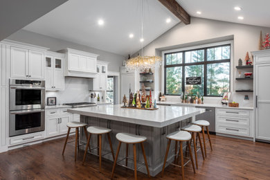 Inspiration for a large transitional l-shaped medium tone wood floor, brown floor and vaulted ceiling open concept kitchen remodel in St Louis with an undermount sink, white cabinets, quartz countertops, white backsplash, quartz backsplash, stainless steel appliances, an island, white countertops and recessed-panel cabinets
