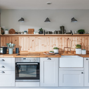 Inspiration for a medium sized rustic open plan kitchen in Hampshire with a belfast sink, recessed-panel cabinets, beige cabinets, wood worktops, wood splashback, stainless steel appliances and light hardwood flooring.