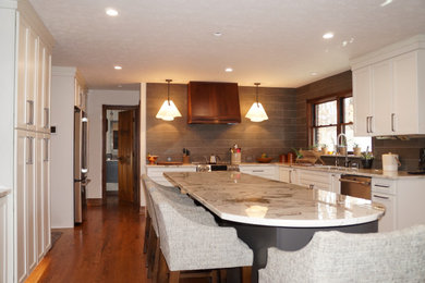 Design ideas for a transitional u-shaped kitchen in Indianapolis with an undermount sink, shaker cabinets, white cabinets, quartzite benchtops, grey splashback, ceramic splashback, stainless steel appliances, medium hardwood floors, with island, brown floor and white benchtop.