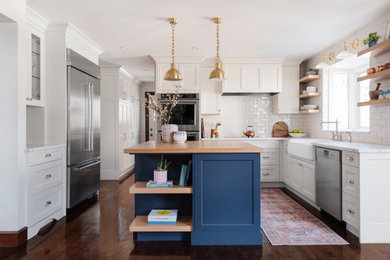 Inspiration for a mid-sized transitional u-shaped dark wood floor and brown floor kitchen remodel in Calgary with a farmhouse sink, shaker cabinets, white cabinets, granite countertops, white backsplash, subway tile backsplash, stainless steel appliances, an island and white countertops