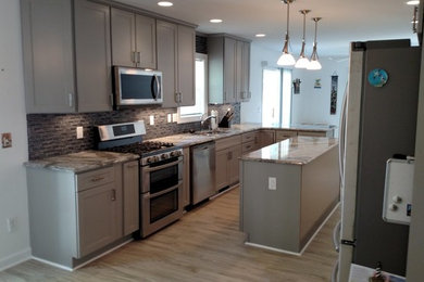Inspiration for a mid-sized craftsman galley light wood floor and beige floor open concept kitchen remodel in Other with a double-bowl sink, recessed-panel cabinets, gray cabinets, granite countertops, brown backsplash, stainless steel appliances, an island and glass tile backsplash
