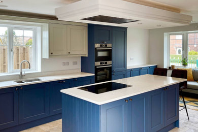 Photo of a large classic single-wall open plan kitchen in Other with a double-bowl sink, shaker cabinets, blue cabinets, quartz worktops, white splashback, black appliances, ceramic flooring, an island, multi-coloured floors, white worktops and a drop ceiling.