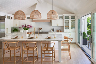 Beach style u-shaped light wood floor, beige floor, shiplap ceiling and vaulted ceiling eat-in kitchen photo in San Francisco with a farmhouse sink, shaker cabinets, white cabinets, marble countertops, white backsplash, stainless steel appliances, an island and multicolored countertops