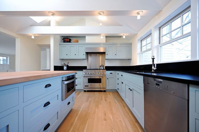 Open concept kitchen - large coastal l-shaped light wood floor open concept kitchen idea in Boston with an undermount sink, recessed-panel cabinets, blue cabinets, wood countertops, black backsplash, stainless steel appliances and an island