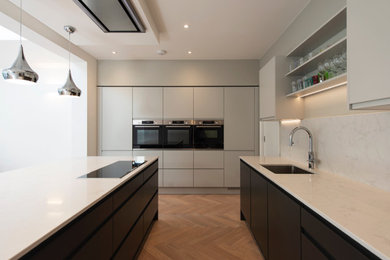 Photo of a medium sized contemporary u-shaped open plan kitchen in London with a submerged sink, flat-panel cabinets, black cabinets, marble worktops, white splashback, marble splashback, integrated appliances, an island, white worktops, a drop ceiling and light hardwood flooring.