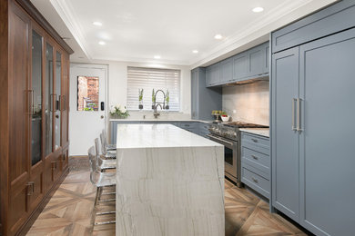 Example of a transitional medium tone wood floor and brown floor kitchen design in Chicago with shaker cabinets, blue cabinets, white backsplash, stainless steel appliances, an island and white countertops