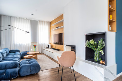 This is an example of a mid-sized contemporary open concept living room in Berlin with blue walls, light hardwood floors, a corner fireplace, a plaster fireplace surround, a wall-mounted tv, beige floor and wood walls.