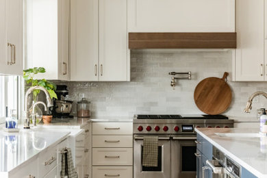 Mid-sized transitional u-shaped medium tone wood floor and multicolored floor open concept kitchen photo in Salt Lake City with a farmhouse sink, recessed-panel cabinets, white cabinets, quartz countertops, white backsplash, subway tile backsplash, stainless steel appliances, an island and white countertops