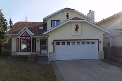 Mid-sized traditional yellow two-story stucco exterior home idea in Calgary with a clipped gable roof