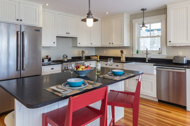 Inspiration for a mid-sized coastal l-shaped medium tone wood floor and multicolored floor eat-in kitchen remodel in Portland Maine with a farmhouse sink, beaded inset cabinets, white cabinets, granite countertops, black backsplash, stainless steel appliances and an island