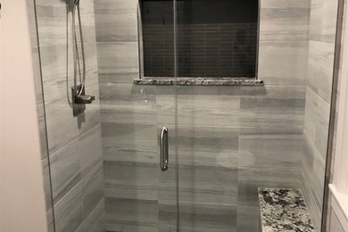 Alcove shower - mid-sized farmhouse master gray tile and porcelain tile porcelain tile and gray floor alcove shower idea in Milwaukee with flat-panel cabinets, gray cabinets, beige walls, a trough sink, granite countertops, a hinged shower door and gray countertops
