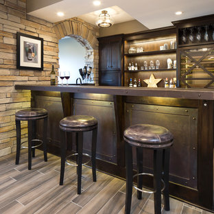 シカゴの中サイズのインダストリアルスタイルのおしゃれな着席型バー (濃色木目調キャビネット、ステンレスカウンター、磁器タイルの床、茶色い床、シェーカースタイル扉のキャビネット) の写真