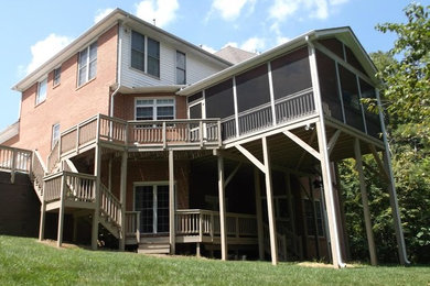 This is an example of a large traditional screened-in and wood railing back porch design in Charlotte with a roof extension.