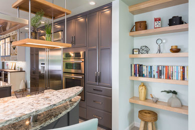 Example of a large mid-century modern l-shaped porcelain tile open concept kitchen design in Manchester with a farmhouse sink, recessed-panel cabinets, gray cabinets, quartz countertops, white backsplash, glass tile backsplash, stainless steel appliances and an island
