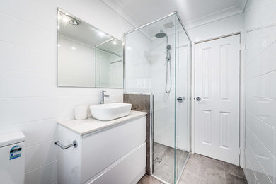 Inspiration for a mid-sized beach style kids bathroom in Perth with furniture-like cabinets, white cabinets, a corner shower, a one-piece toilet, white tile, ceramic tile, white walls, porcelain floors, a vessel sink, solid surface benchtops, grey floor, a hinged shower door and white benchtops.
