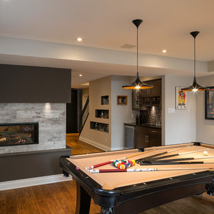 Inspiration for a medium sized contemporary fully buried basement in Ottawa with beige walls, laminate floors, a two-sided fireplace, a tiled fireplace surround and brown floors.