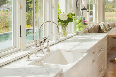 Example of a large beach style light wood floor eat-in kitchen design in New York with a farmhouse sink, recessed-panel cabinets, white cabinets, marble countertops, white countertops and window backsplash