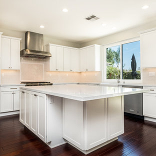 Photo of a mid-sized transitional u-shaped kitchen pantry in Orange County with a farmhouse sink, shaker cabinets, white cabinets, quartz benchtops, white splashback, porcelain splashback, stainless steel appliances, cork floors, with island, brown floor and white benchtop.