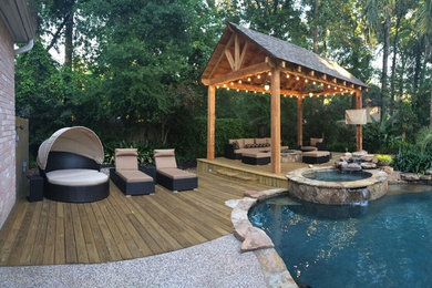Design ideas for a mid-sized tropical backyard custom-shaped natural pool in Houston with a hot tub and natural stone pavers.