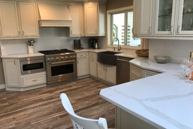 Mid-sized transitional u-shaped open plan kitchen in New York with a farmhouse sink, shaker cabinets, white cabinets, marble benchtops, white splashback, ceramic splashback, stainless steel appliances, medium hardwood floors and a peninsula.