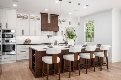 Large transitional l-shaped light wood floor and brown floor eat-in kitchen photo in Columbus with an undermount sink, flat-panel cabinets, white cabinets, quartz countertops, white backsplash, ceramic backsplash, stainless steel appliances, an island and black countertops