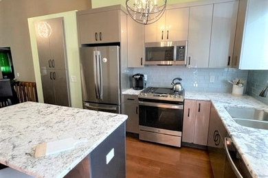Example of a large minimalist l-shaped medium tone wood floor and brown floor eat-in kitchen design in Detroit with an undermount sink, flat-panel cabinets, beige cabinets, granite countertops, blue backsplash, glass tile backsplash, stainless steel appliances, an island and gray countertops