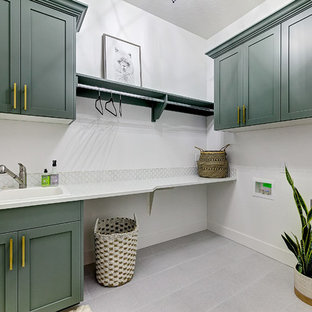 Imagen de cuarto de lavado en L, campestre, grande, con fregadero encastrado, armarios estilo shaker, puertas de armario verdes, encimera de cuarzo compacto, paredes blancas, suelo de baldosas de porcelana, lavadora y secadora juntas, suelo gris y encimeras blancas