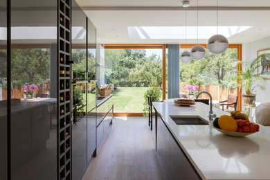 Photo of a medium sized contemporary grey and white single-wall kitchen/diner in London with a submerged sink, grey cabinets, quartz worktops, white splashback, stone slab splashback, integrated appliances, medium hardwood flooring, an island, white worktops and all types of ceiling.