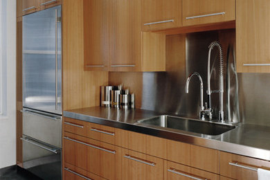 Photo of a contemporary kitchen in New York with an integrated sink, flat-panel cabinets, medium wood cabinets, stainless steel benchtops, stainless steel appliances, metallic splashback and metal splashback.