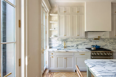 Inredning av ett klassiskt mellanstort vit vitt kök, med en undermonterad diskho, luckor med profilerade fronter, grå skåp, marmorbänkskiva, stänkskydd i marmor, rostfria vitvaror, mellanmörkt trägolv, en köksö, brunt golv och vitt stänkskydd