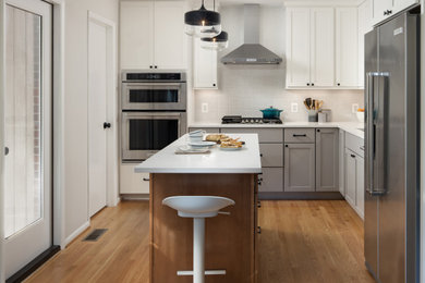 Eat-in kitchen - mid-sized 1950s l-shaped medium tone wood floor and brown floor eat-in kitchen idea in DC Metro with an undermount sink, shaker cabinets, white cabinets, quartz countertops, white backsplash, ceramic backsplash, stainless steel appliances, an island and white countertops