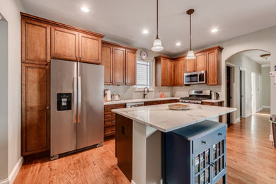 Example of a mid-sized transitional l-shaped medium tone wood floor and brown floor eat-in kitchen design in St Louis with a double-bowl sink, raised-panel cabinets, dark wood cabinets, quartz countertops, green backsplash, stone tile backsplash, stainless steel appliances, an island and white countertops