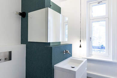 Kleines Modernes Duschbad mit flächenbündigen Schrankfronten, weißen Schränken, Einbaubadewanne, Duschbadewanne, Wandtoilette, grünen Fliesen, Mosaikfliesen, weißer Wandfarbe, Wandwaschbecken, Mineralwerkstoff-Waschtisch, grauem Boden, offener Dusche und weißer Waschtischplatte in Hamburg