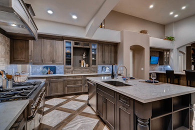 This is an example of a mediterranean kitchen in Phoenix with an undermount sink, recessed-panel cabinets, quartzite benchtops, travertine splashback, stainless steel appliances, porcelain floors and with island.
