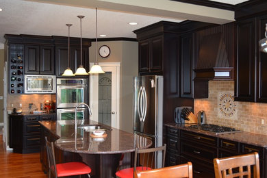 Large elegant u-shaped medium tone wood floor eat-in kitchen photo in Calgary with an undermount sink, raised-panel cabinets, black cabinets, granite countertops, beige backsplash, stone tile backsplash, stainless steel appliances and an island