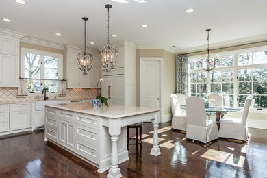 Large transitional u-shaped medium tone wood floor and brown floor open concept kitchen photo in Raleigh with a farmhouse sink, recessed-panel cabinets, white cabinets, quartzite countertops, beige backsplash, stone tile backsplash, paneled appliances, an island and white countertops