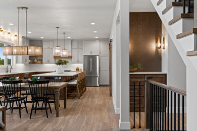 Large transitional l-shaped vinyl floor and brown floor eat-in kitchen photo in Other with an undermount sink, shaker cabinets, brown cabinets, quartz countertops, white backsplash, porcelain backsplash, stainless steel appliances, an island and white countertops