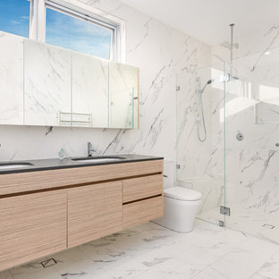Inspiration for a contemporary master bathroom in Newcastle - Maitland with flat-panel cabinets, light wood cabinets, an alcove shower, a one-piece toilet, white tile, marble floors, an undermount sink, white floor, a hinged shower door and black benchtops.